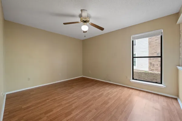 an empty room with wooden floor chandelier fan and windows