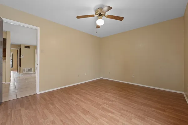 an empty room with wooden floor chandelier fan and windows