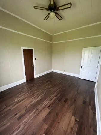 a view of an empty room with wooden floor and a ceiling fan