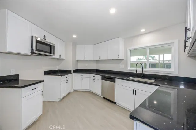 a kitchen with granite countertop a sink stainless steel appliances and white cabinets