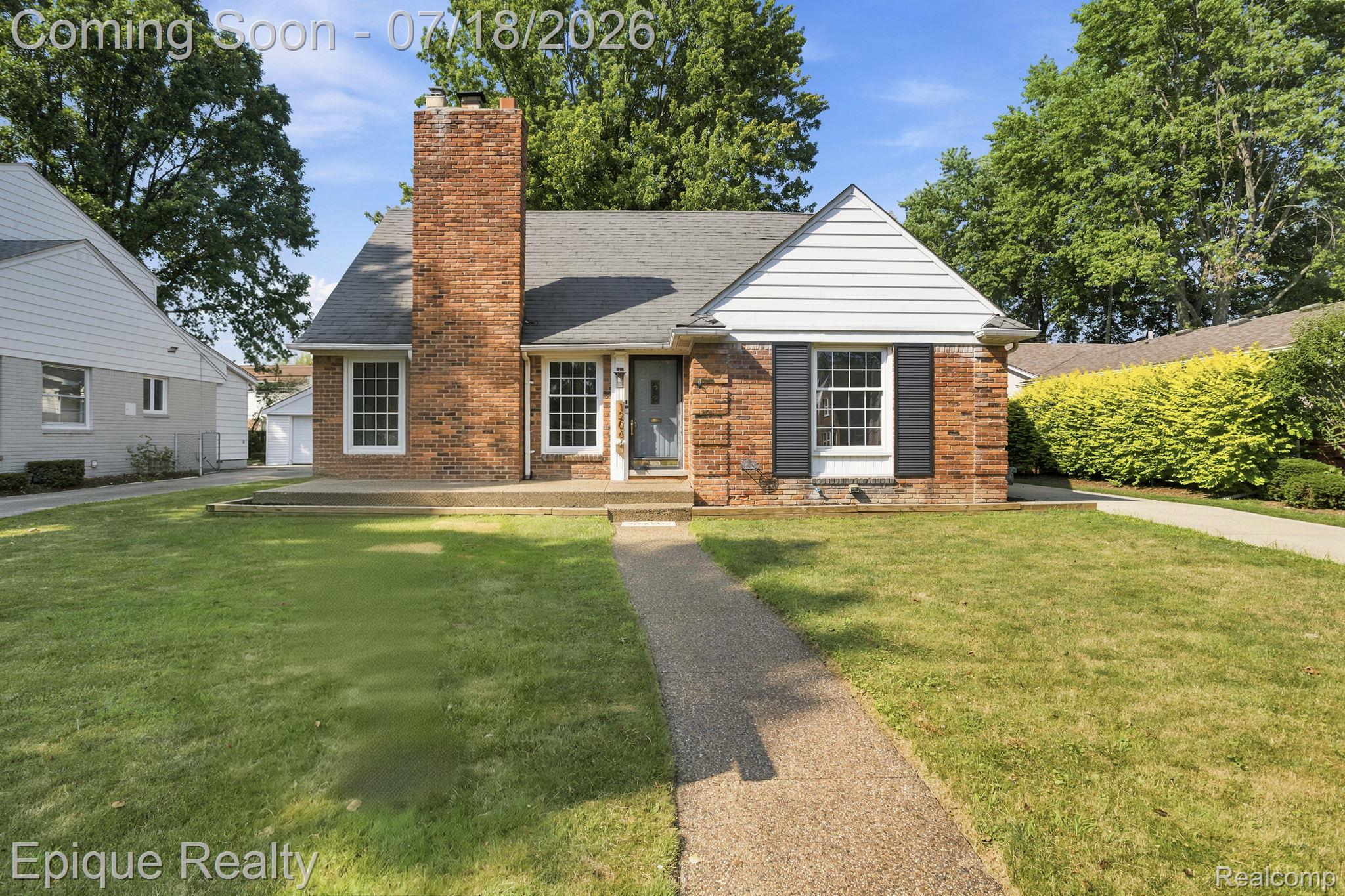 Traditional brick facade residence featuring a prominent brick chimney, white gabled accents, dark louvered shutters, a front entry path, and established lawn space