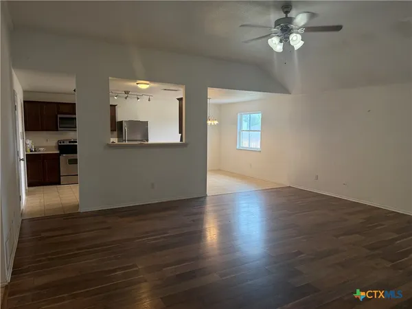 an empty room with wooden floor chandelier fan and windows