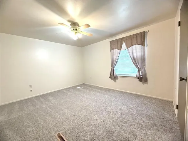 an empty room with a chandelier fan and wooden floor
