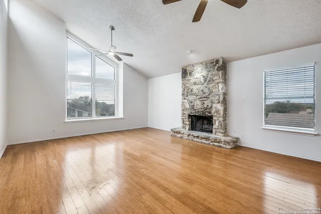 a view of an empty room with wooden floor fireplace and a window