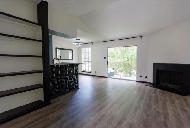 a view of an empty room with wooden floor fireplace and a window