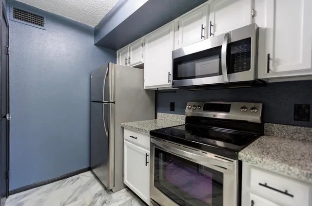 a kitchen with stainless steel appliances granite countertop white cabinets and a stove top oven