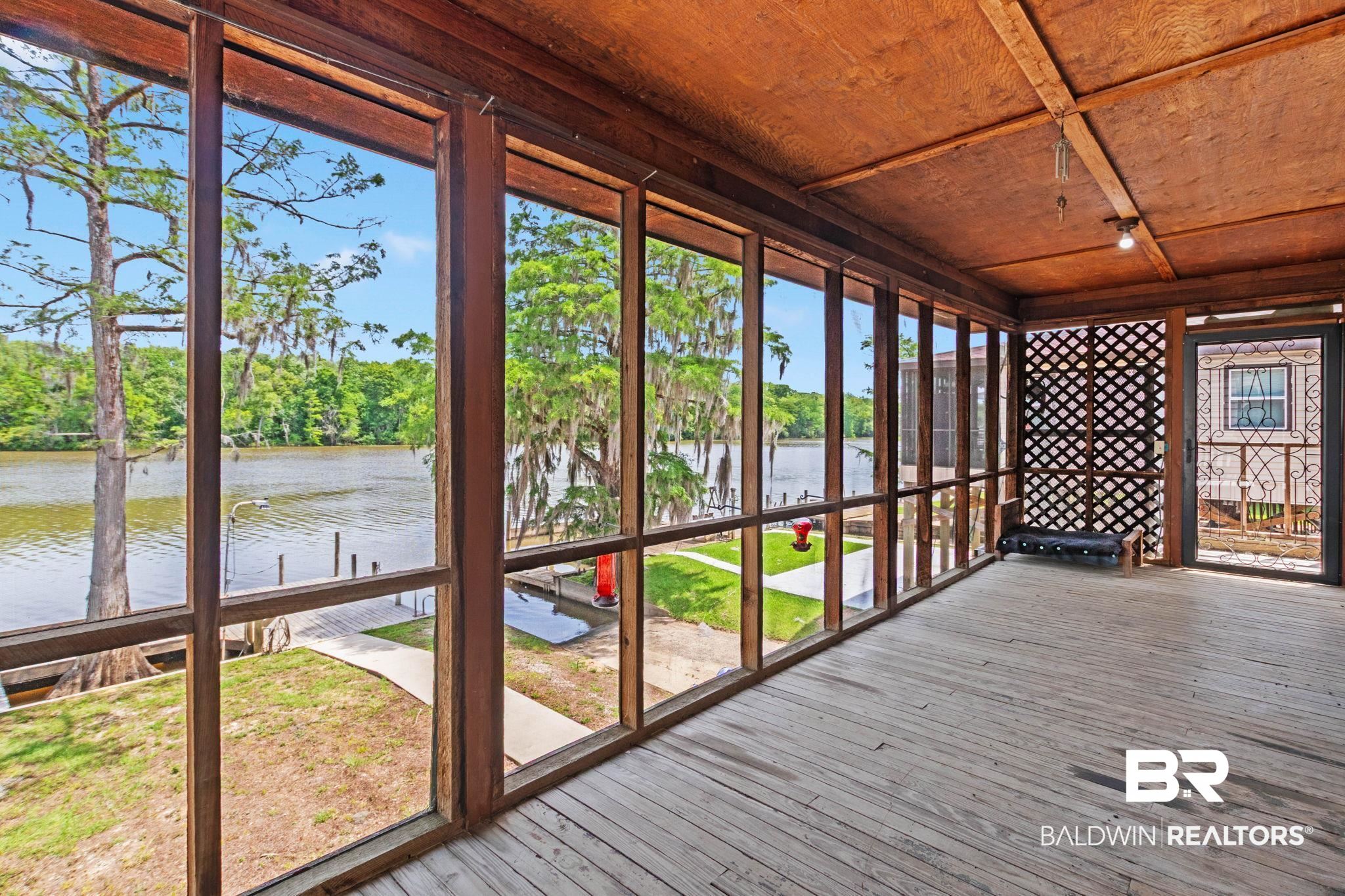 8153 Bryant's Lndg Road Stockton, AL 36579 - Photo 4 of 87 Screened porch with wood-finish walls and ceilings, featuring an expansive water frontage, a private dock with pilings, and a concrete pathway leading to the water