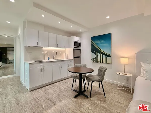a kitchen with stainless steel appliances kitchen island granite countertop a dining table chairs and a refrigerator