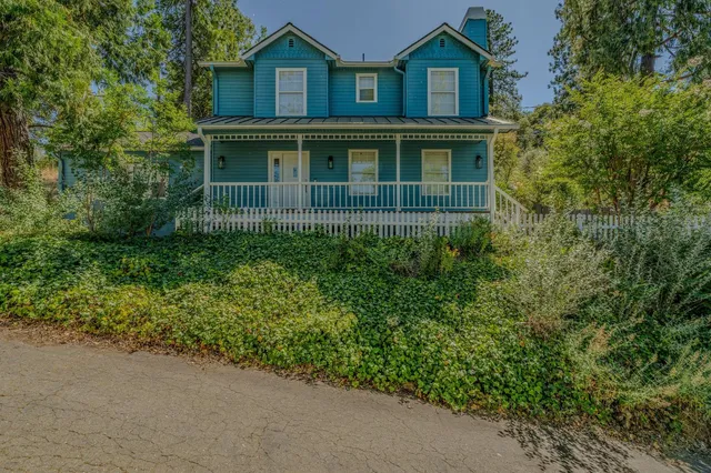 a view of a brick house with large windows and a yard with plants and large trees