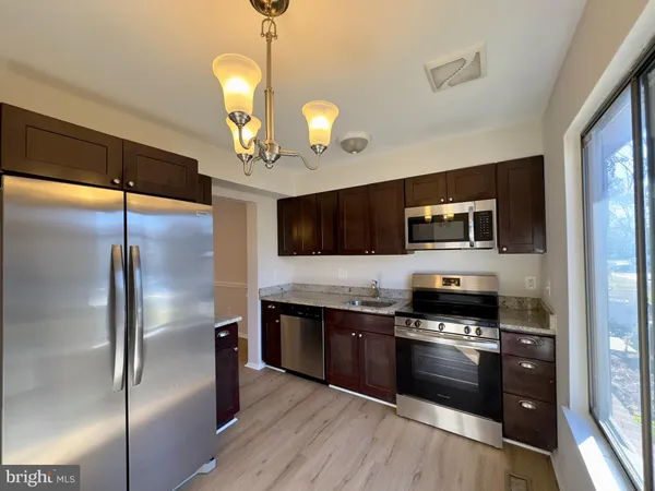 a kitchen with stainless steel appliances a stove top oven a refrigerator and a sink with wooden floor