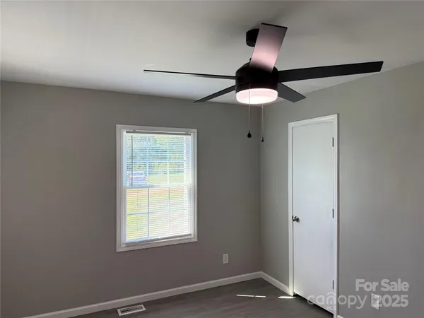 a view of an empty room with window and chandelier fan