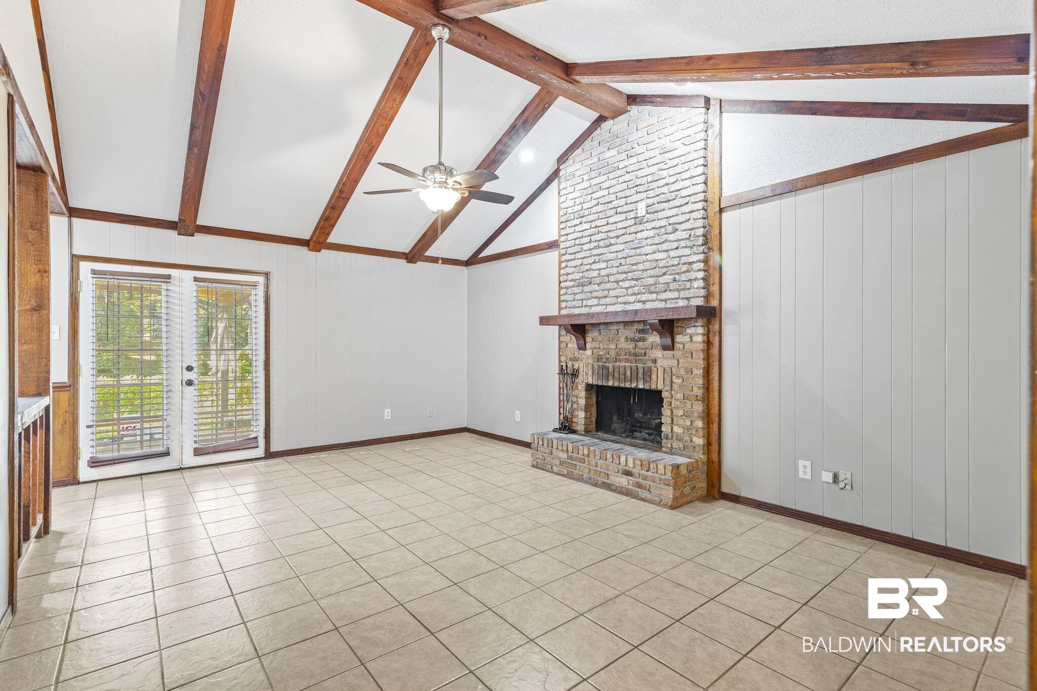 4151 Springdale Road Mobile, AL 36609 - Photo 4 of 21 Unfurnished living room featuring a fireplace, wooden walls, vaulted ceiling with beams, light tile patterned floors, and ceiling fan