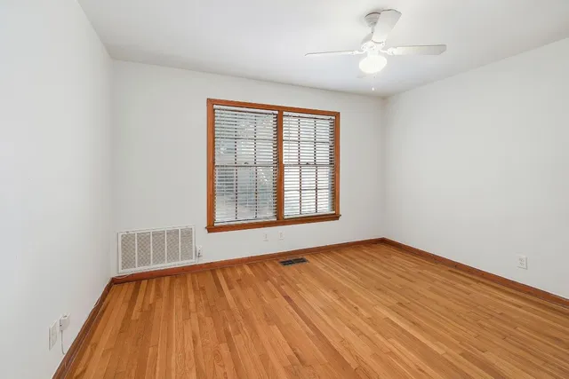 an empty room with wooden floor chandelier fan and windows
