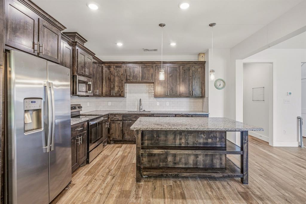 745 North Miller Avenue Stephenville, TX 76401 - Photo 10 of 31 Kitchen featuring wood-finish flooring, dark wood cabinetry, stainless steel appliances, granite countertops, and a subway tile backsplash