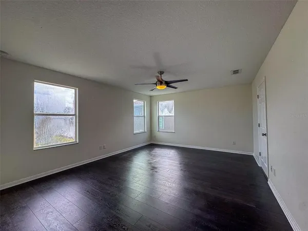 an empty room with wooden floor chandelier and windows