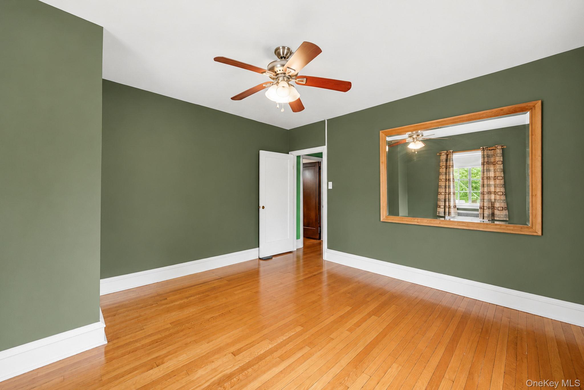 18240 Avon Road Queens, NY 11432 - Photo 10 of 30 Spacious room featuring wood-finish flooring, a ceiling fan with integrated lighting, and a large wall-mounted mirror with a wood frame