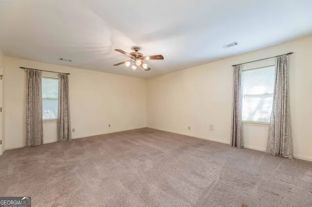 an empty room with chandelier fan and windows