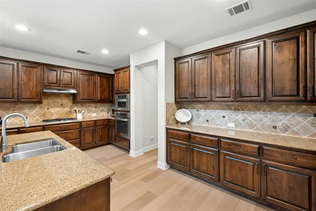 a kitchen with stainless steel appliances granite countertop a stove a sink dishwasher a refrigerator and wooden cabinets with wooden floor