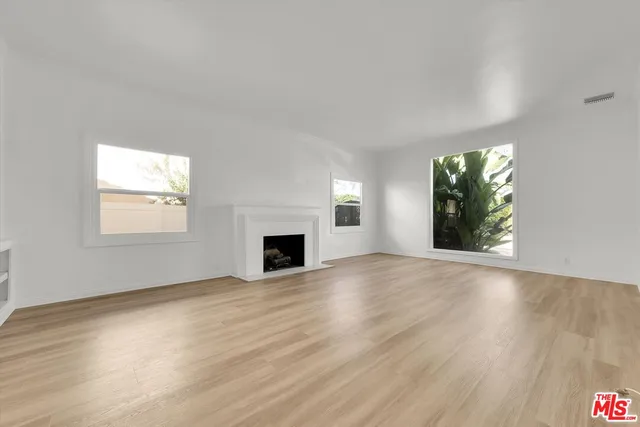 an empty room with wooden floor fireplace and windows