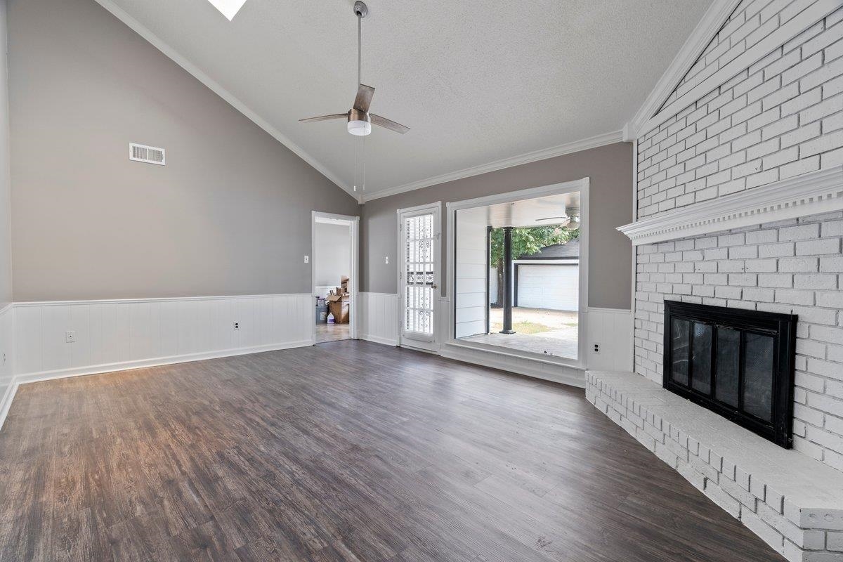 Unfurnished living room with ceiling fan, vaulted ceiling, crown molding, and dark hardwood / wood-style floors