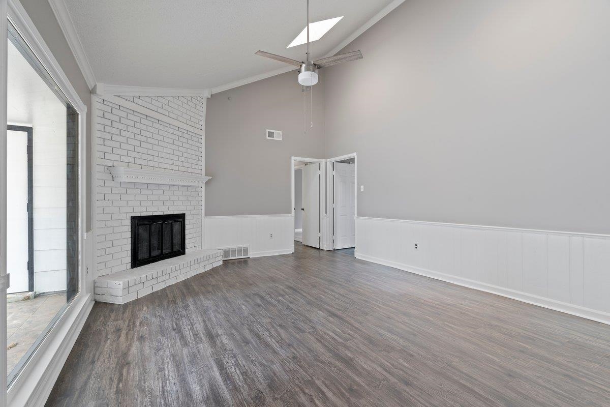 Unfurnished living room featuring a fireplace, crown molding, dark wood-type flooring, and lofted ceiling with skylight