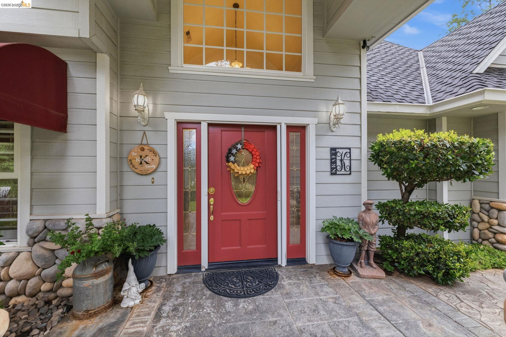 18450 Lambert Lake Road Sonora, CA 95370 - Photo 72 of 87 Entryway featuring a red paneled door with sidelights, transom window, stamped concrete porch, stone veneer accents, and established landscaping