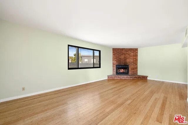 an empty room with wooden floor fireplace and windows