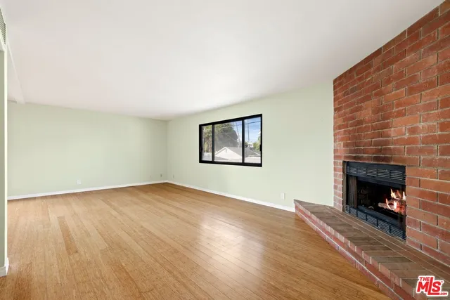 a view of an empty room with wooden floor fireplace and a window