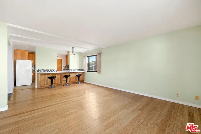 a view of an empty room with wooden floor and a kitchen view