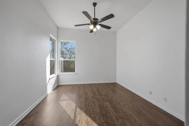 an empty room with wooden floor fan and windows