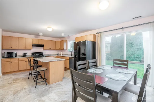 a kitchen with a refrigerator a stove a sink dishwasher with a dining table and chairs with outer view