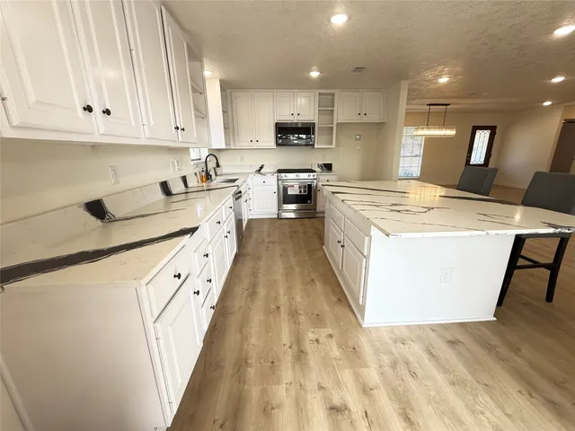 a kitchen with stainless steel appliances granite countertop a stove a sink and white cabinets with wooden floor