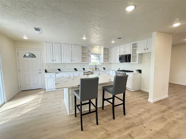 a kitchen with kitchen island a dining table chairs and white cabinets