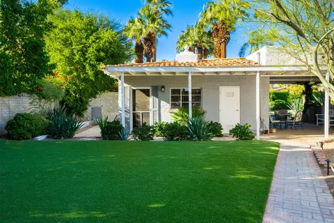 a view of a white house with a big yard and potted plants and large trees