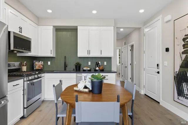 a kitchen with stainless steel appliances granite countertop a stove top oven a refrigerator a sink and a dining table with white cabinets