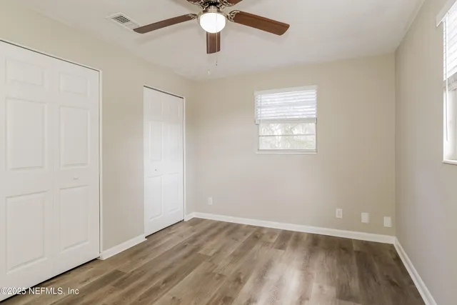 an empty room with wooden floor fan and windows