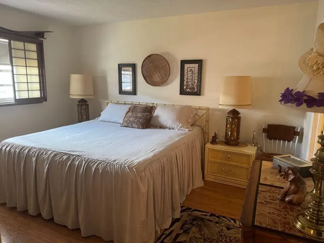 a bedroom with a bed and a lamp on dresser next to a window