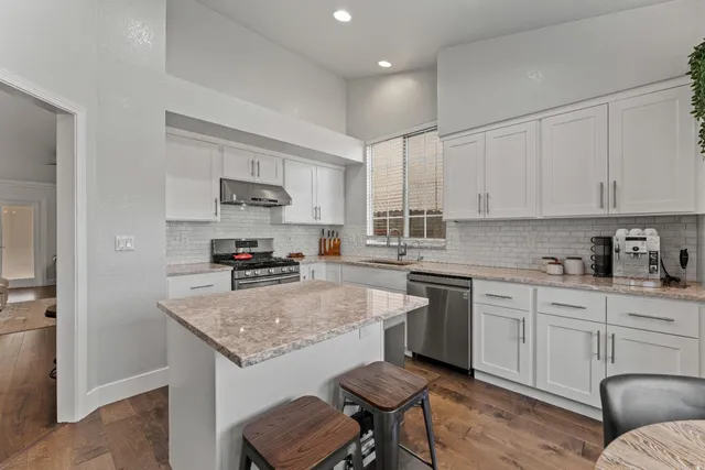 a kitchen with granite countertop kitchen island a sink stove and white cabinets
