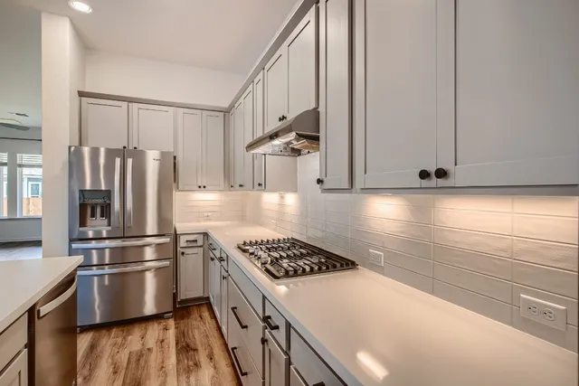 a kitchen with stainless steel appliances a refrigerator a stove a sink cabinets and wooden floor