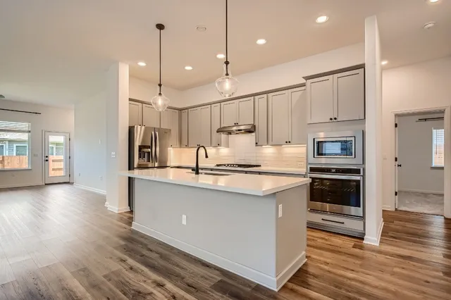 a kitchen with stainless steel appliances granite countertop a refrigerator a oven a sink and white cabinets with wooden floor