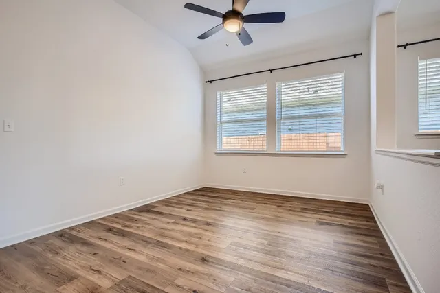 an empty room with wooden floor fan and windows