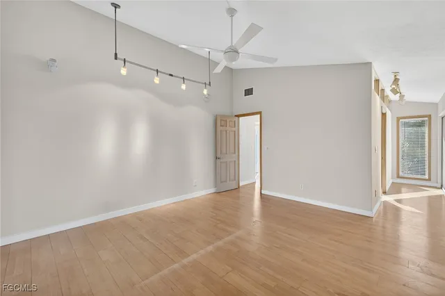 a view of an empty room with wooden floor and a ceiling fan