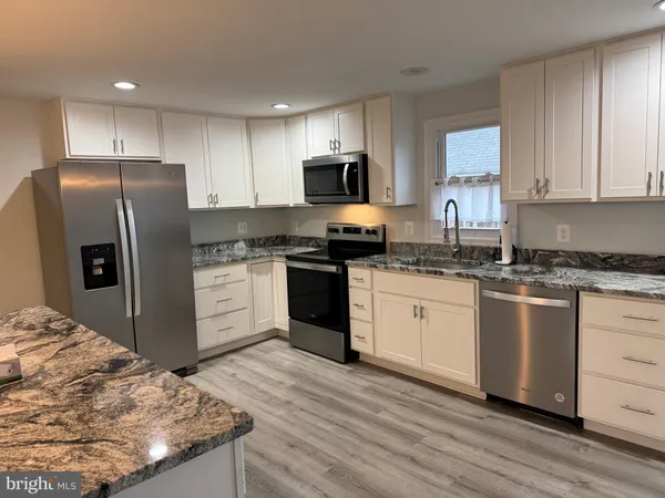 a kitchen with granite countertop a refrigerator sink and white cabinets