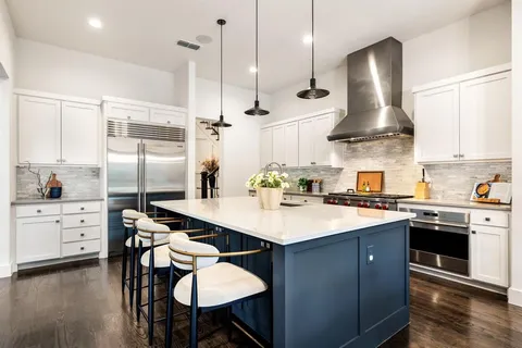 a kitchen with stainless steel appliances a sink a stove a refrigerator and white cabinets with wooden floor