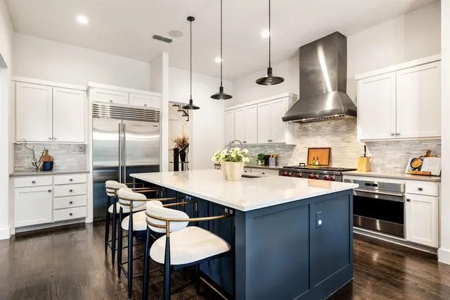 a kitchen with stainless steel appliances a sink a stove a refrigerator and white cabinets with wooden floor