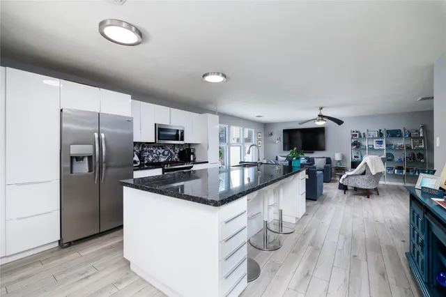 a kitchen with stainless steel appliances granite countertop a refrigerator a sink dishwasher a stove and a microwave oven on the wooden floor