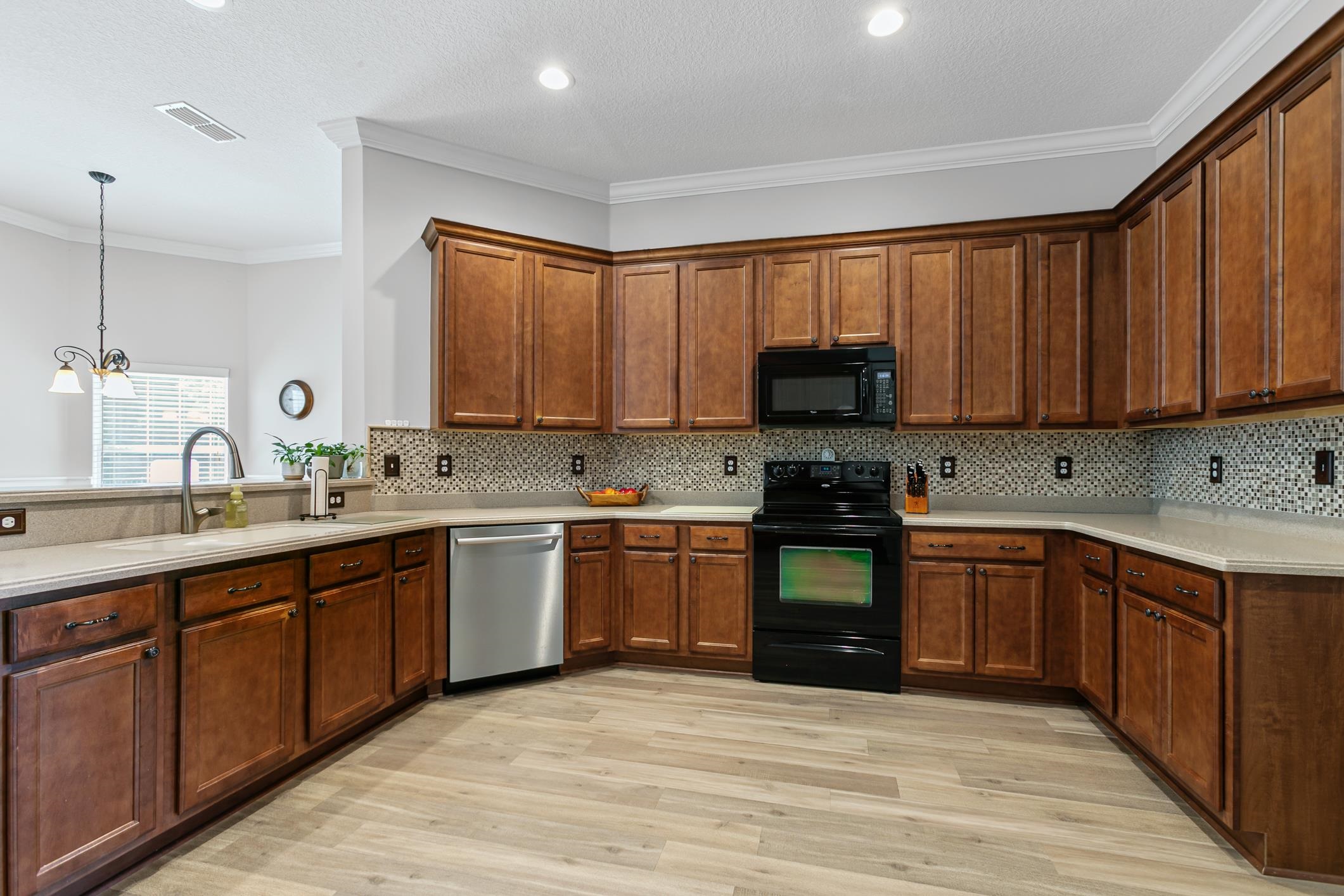2724 North Portofino Road St. Augustine, FL 32092 - Photo 24 of 86 Kitchen featuring black appliances, crown molding, light wood-style flooring, hanging light fixtures, and decorative backsplash