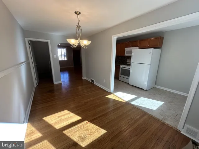 a view of a refrigerator in kitchen and an empty room with wooden floor