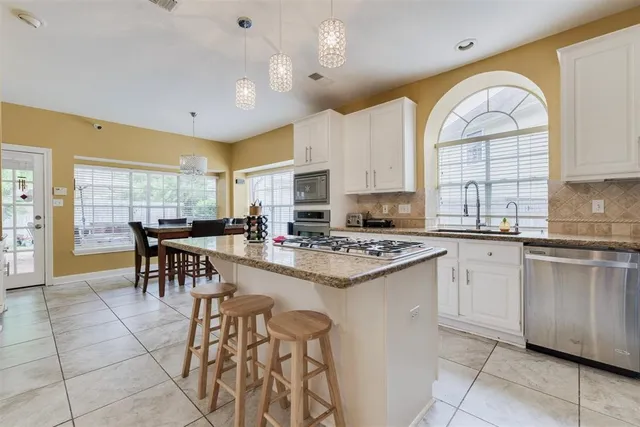 a kitchen with stainless steel appliances granite countertop a stove top oven a sink a dining table and chairs with a large window