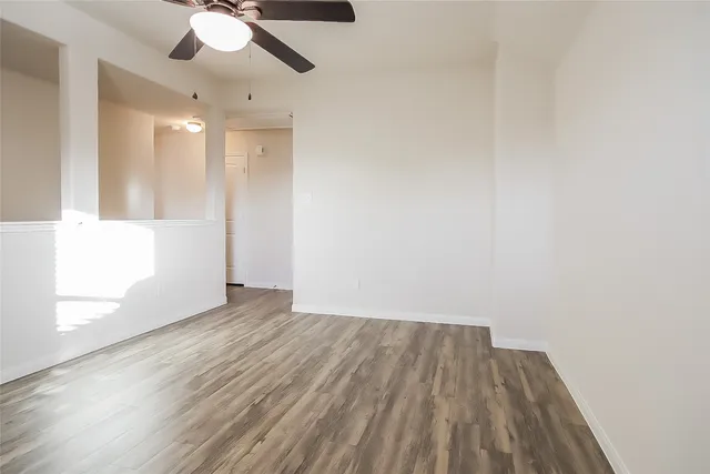 a view of an empty room with wooden floor and a ceiling fan